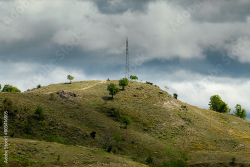 Electric pole on top of a hill with dramatic backgorund cloudy sky.