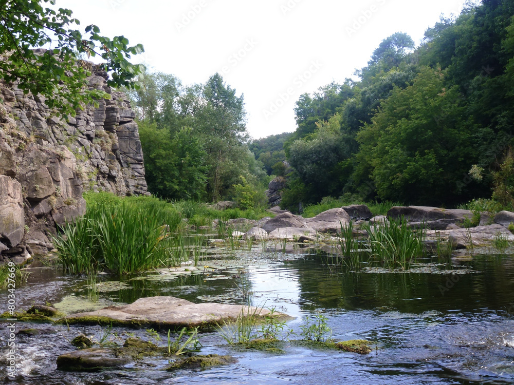 The stony slopes of the former quarry were filled with water and a lake was formed. Grass and stones are reflected in the water