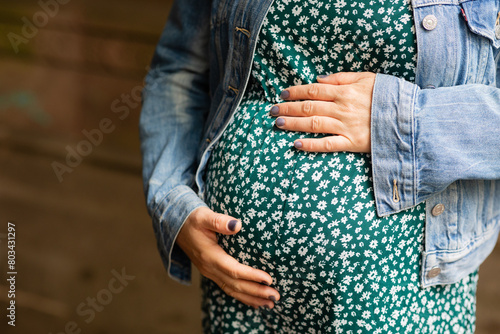 closeup of torso of pregnant woman in green floral dress holding her pregnant belly