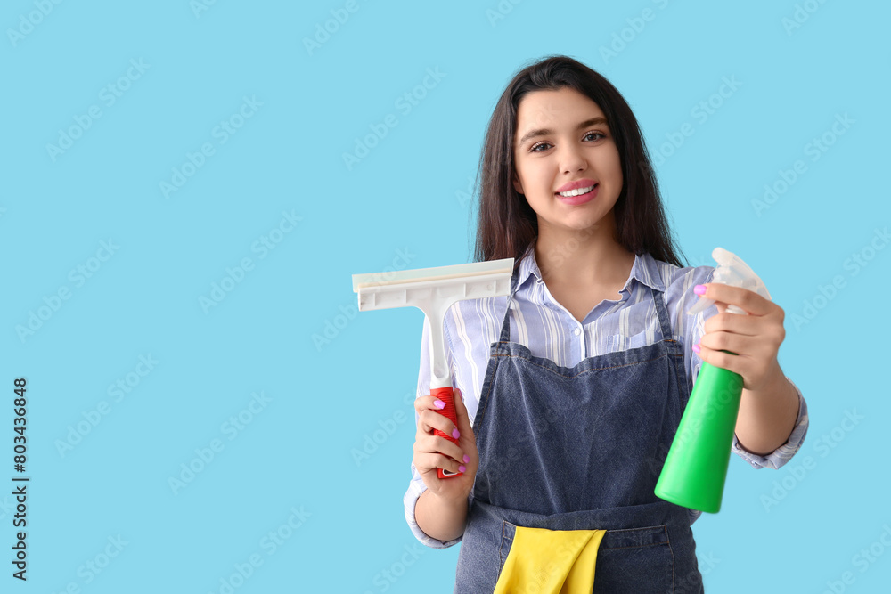 Young woman with squeegee and detergent on blue background Young woman with squeegee and detergent on blue background