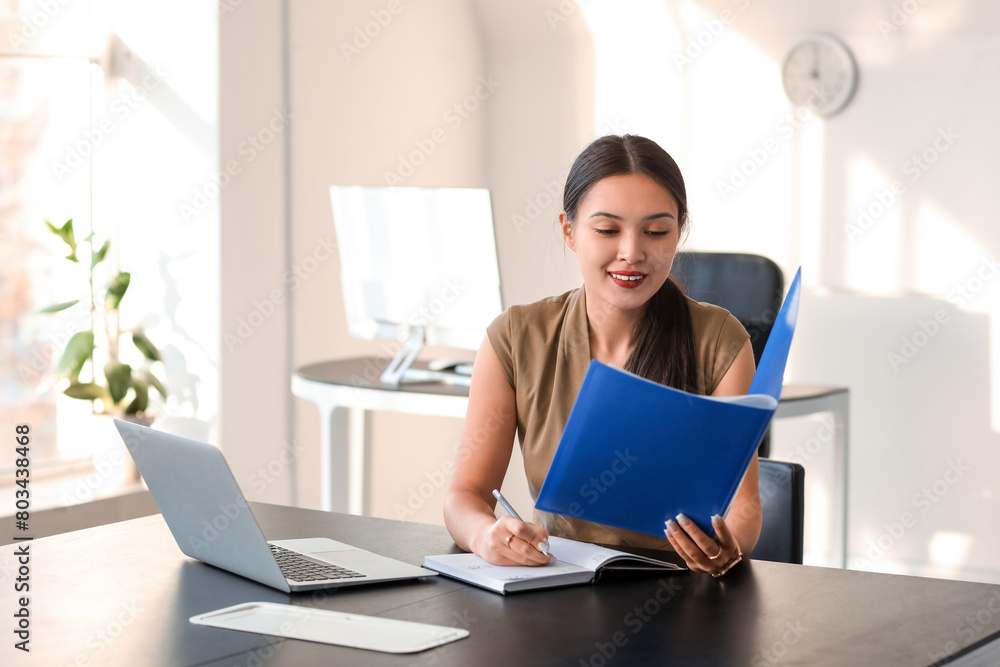 Obraz premium Young Asian businesswoman with folder and notebook working at table in office