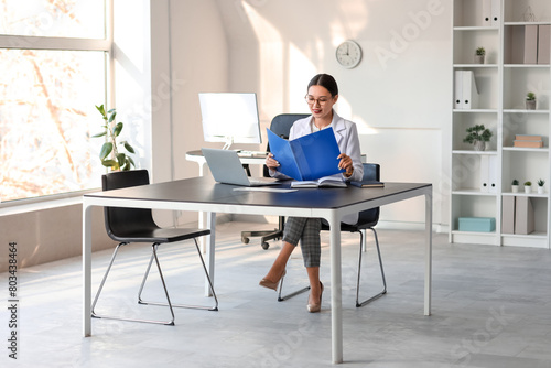 Young Asian businesswoman with folder working at table in office