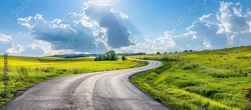 Beautiful countryside landscape with an asphalt road winding through a summer field under a blue cloudy sky.