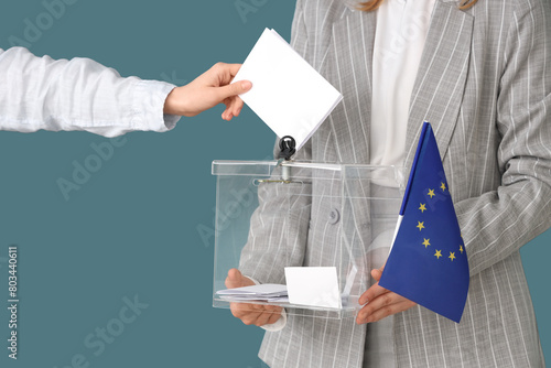 Hand putting voting paper into ballot box on blue background. Election concept photo