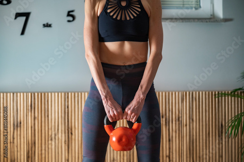 Front view of a fit woman working out at home holding a kettlebell weight