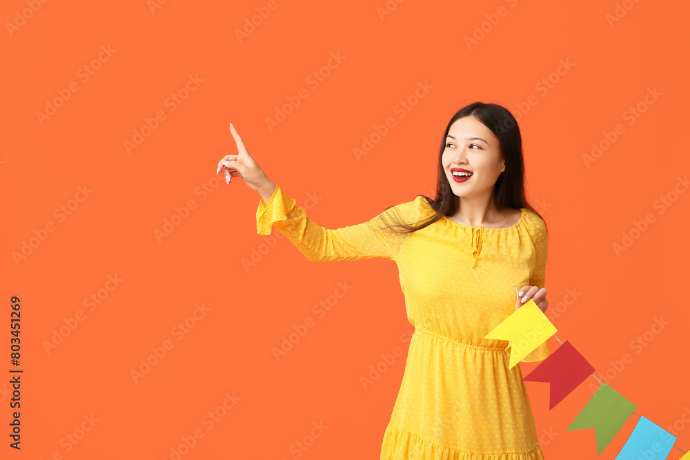 Happy young woman with festive garland pointing at something on orange background Happy young woman with festive garland pointing at something on orange background