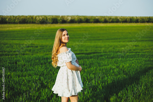 A smiling pregnant woman in a white light dress walks in a green spring garden. A woman is expecting a child. Happy pregnant woman in nature.