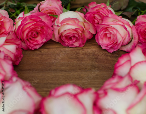 A bouquet of pink and white roses arranged in a heart shape on a wooden surface.
