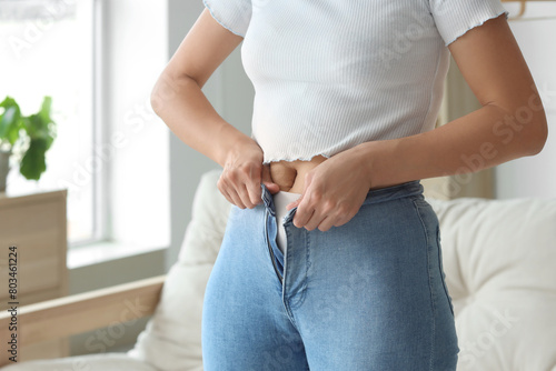 Young woman trying to button tight pants at home, closeup. Diet concept photo