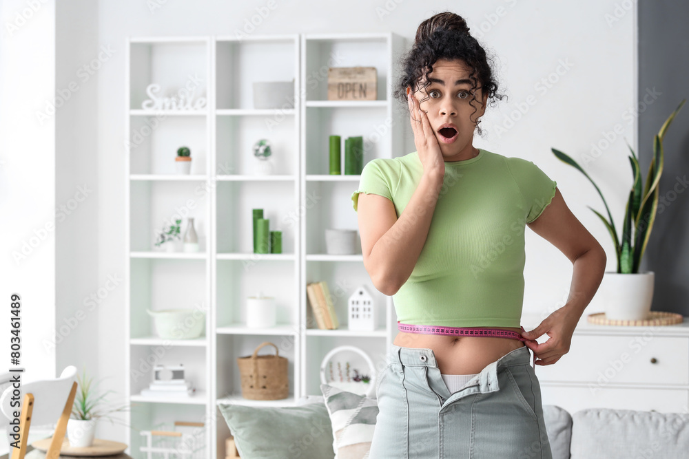 Shocked African-American woman in tight skirt measuring her waist at home. Diet concept Shocked African-American woman in tight skirt measuring her waist at home. Diet concept