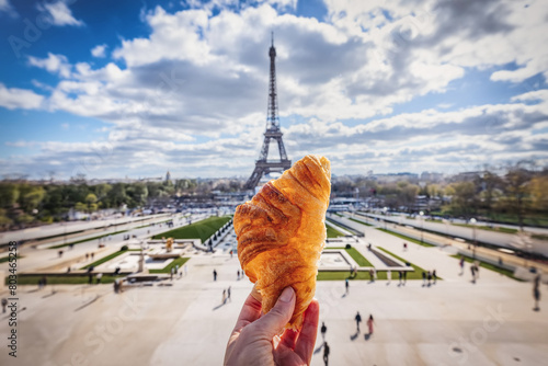 A hand holding a french Croissant in front of the Eiffel Tower in Paris as travel concept for France