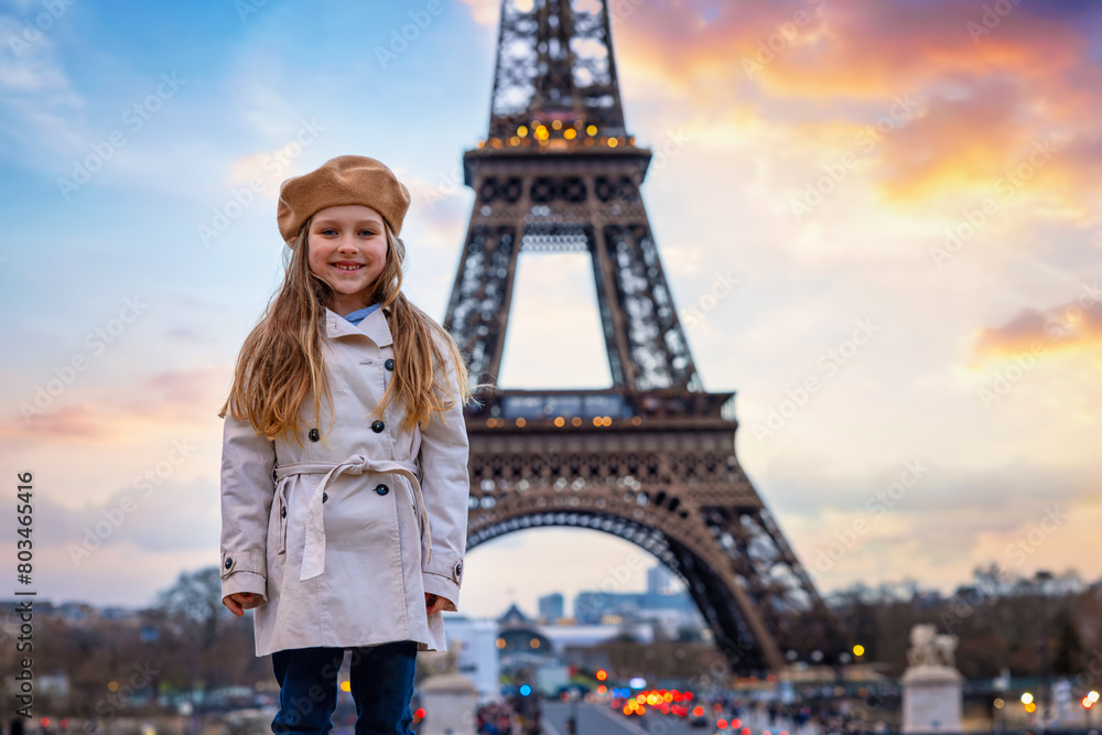 Portrait of a cute, blonde girl with a trench coat and a beret hat in front of the Eiffel Tower in Paris, France