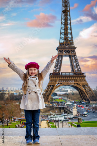 A happy, cute girl with a trench coat and a beret hat in front of the Eiffel Tower in Paris, France, during sunset time © moofushi