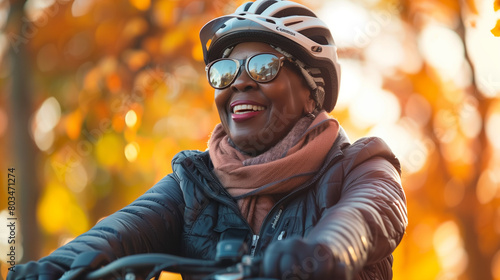 A joyful African American woman wearing a helmet and sunglasses rides a bicycle in an autumn park. © Another vision