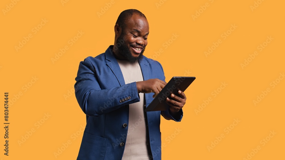 Smiling man scrolling on tablet touchscreen, using internet and credit card to pay for products. African american person happily browsing online shopping websites, studio background, camera B Smiling man scrolling on tablet touchscreen, using internet and credit card to pay for products. African american person happily browsing online shopping websites, studio background, camera B