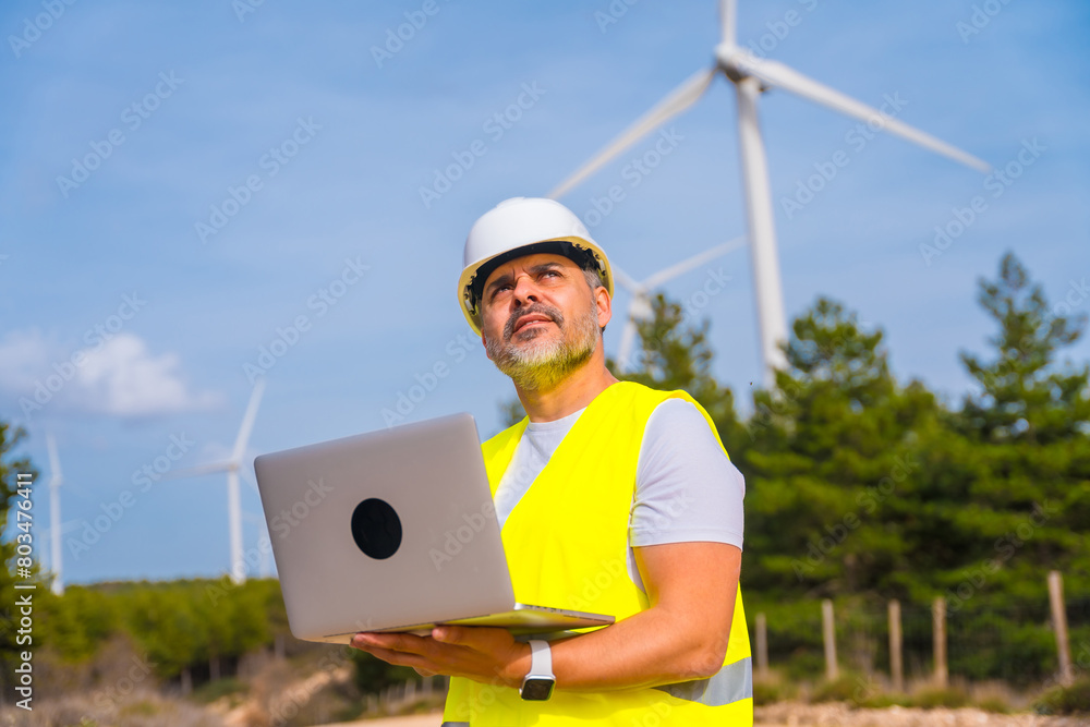 Man using laptop standing in a wind turbine field Man using laptop standing in a wind turbine field