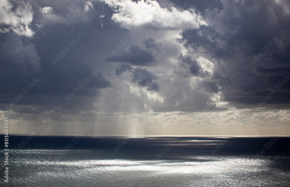 Obraz premium Overcast grey sky with low textured clouds. Sunlight peeks through the clouds and falls on the sea. Background. Horizontal