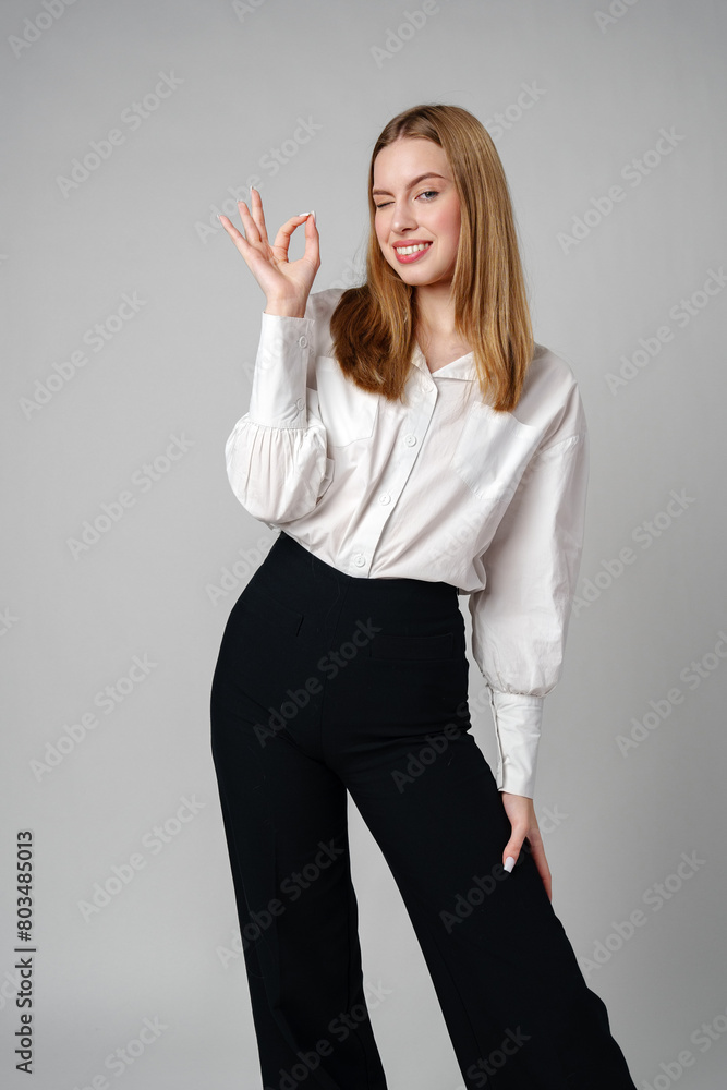Young Woman Gesturing OK Sign With Hand Against a Neutral Background Young Woman Gesturing OK Sign With Hand Against a Neutral Background