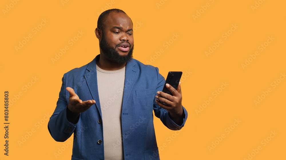Upbeat man having friendly conversation with friends during teleconference meeting using smartphone, studio background. BIPOC person has fun catching up with mates during online videocall, camera A Upbeat man having friendly conversation with friends during teleconference meeting using smartphone, studio background. BIPOC person has fun catching up with mates during online videocall, camera A