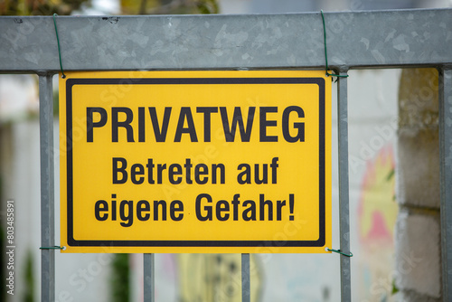 Yellow warning sign with the German inscription "Privatweg! Enter at your own risk". Outdoor, fence, nobody. 