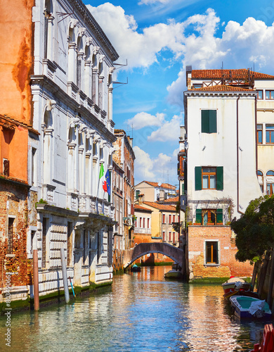 Venice, Italy. Antique stone bridge on the canal with boats and motorboats among old town italian houses. Sunny summer day. Picturesque landscape