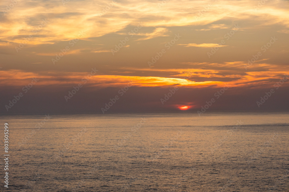 Landscape photo of dramatic, steep orange cliffs by the atlantic at sunset. Shot in Farol fo Cabo de Sao Vincente near Sagres, Portugal.