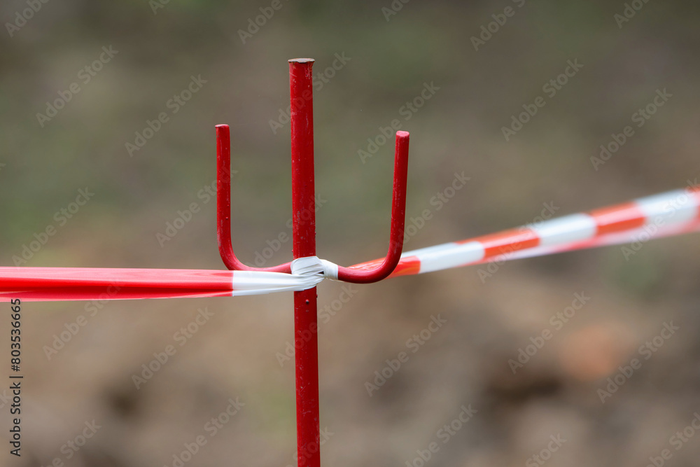 a red and white barrier tape is attached to a red bollard in front of a blurred brown background a red and white barrier tape is attached to a red bollard in front of a blurred brown background