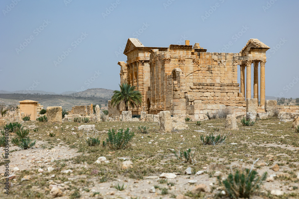 Well-preserved golden hued stone ruins of Capitoline Temples standing majestically in antique Roman forum of Sbeitla on sunny spring day, Tunisia