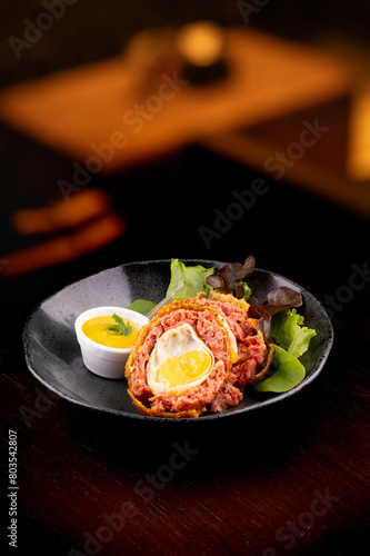 scotch egg with green salad and yellow mustard on plate on blurred background