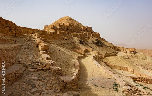 Scenic view of sun-drenched ancient abandoned stone Berber troglodyte dwellings of Ksar Guermassa on arid hillsides of Jebel Dahar mountain range in Tunisia