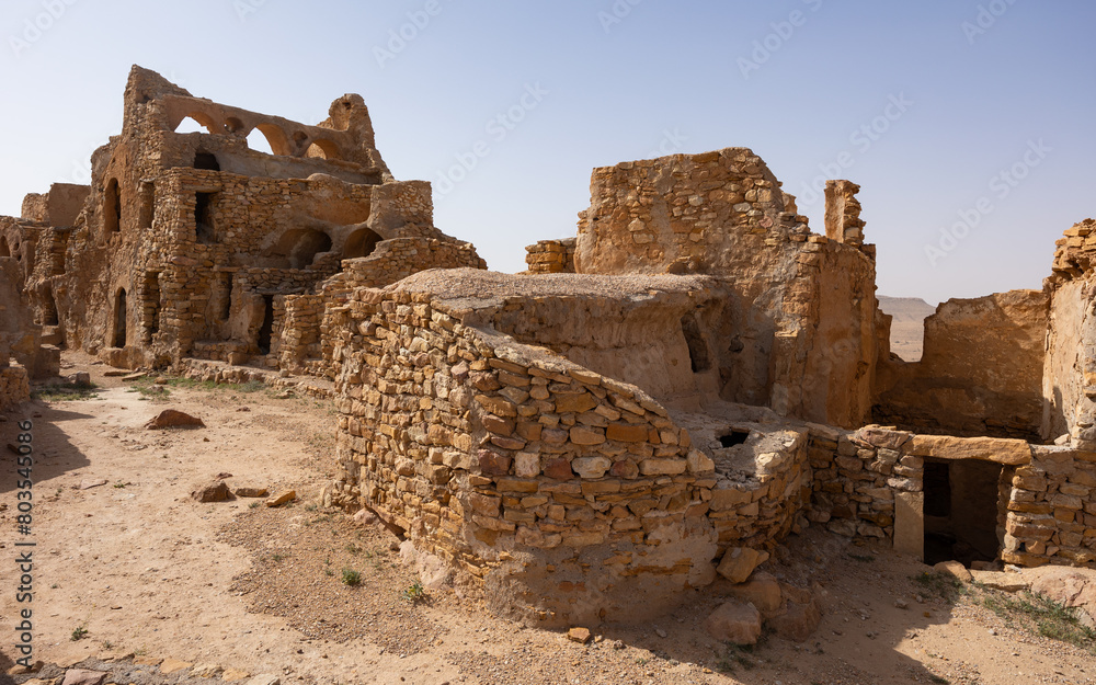 Eroded stone walls and arches of fortifications of Ksar Beni Barka standing under blue Tunisian sky, showcasing traditional Berber architecture in Tataouine