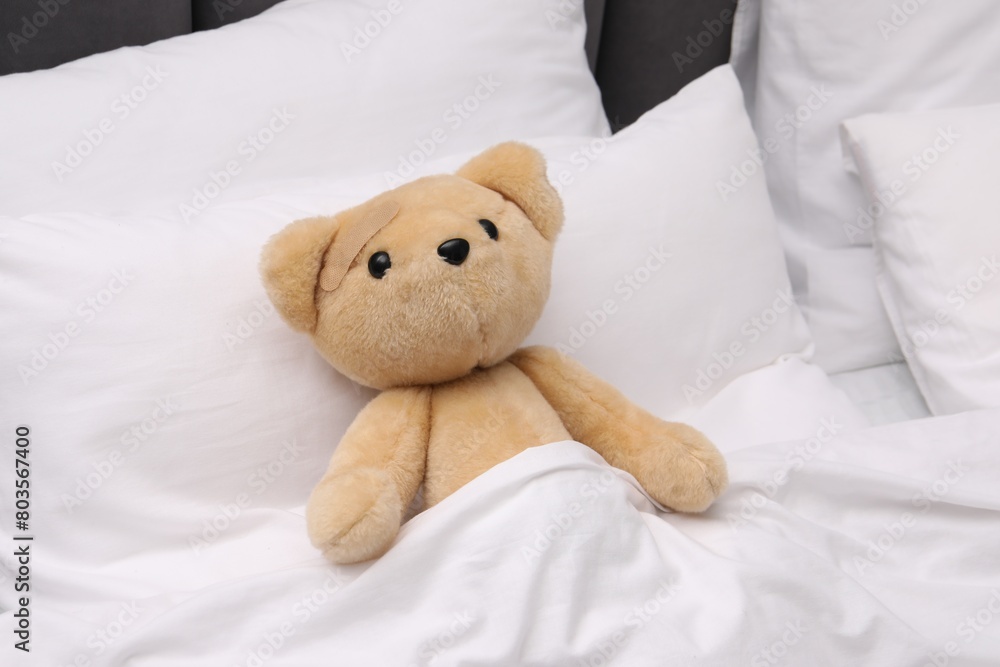 Toy cute bear with sticking plaster under blanket in bed