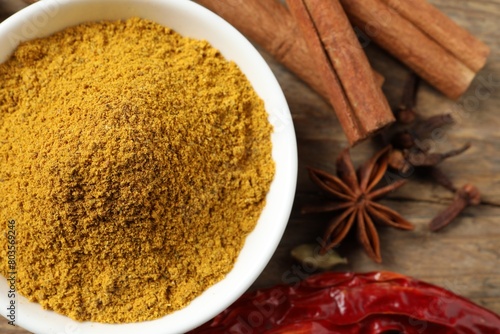 Dry curry powder in bowl and other spices on wooden table, flat lay