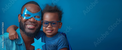 Happy African American father and son wearing matching blue outfits and superhero masks, celebrating Father's Day photo