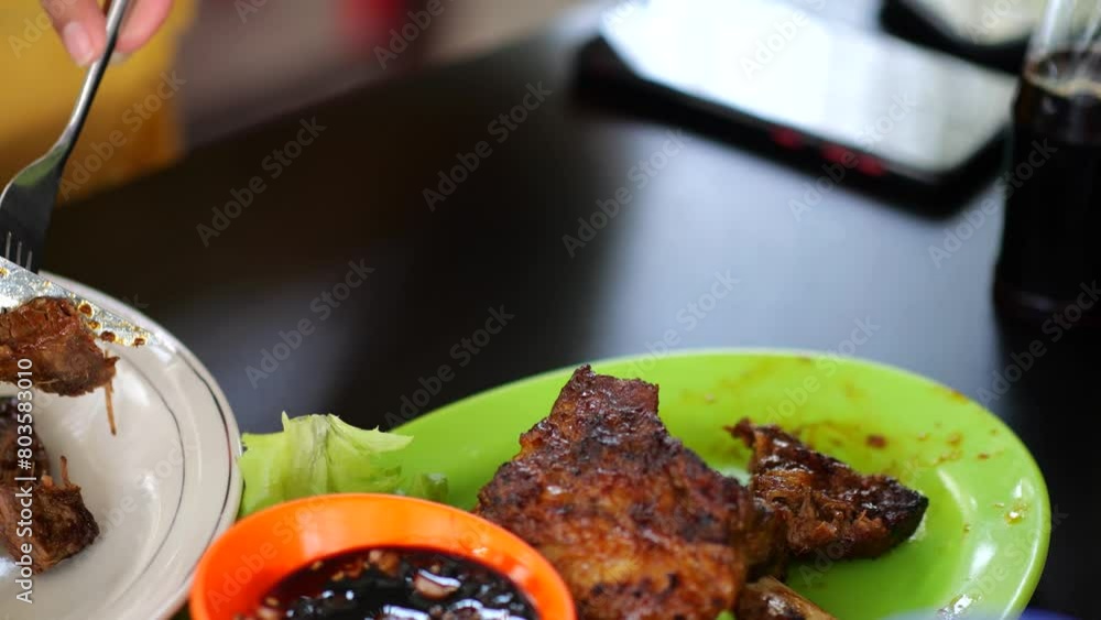 Indonesian woman in a restaurant eating beef rib steak fried on a barbecue grill. Eating barbecue rib. Grilled pork ribs. Tasty food. Delicious juicy pork ribs on a barbecue grill.
Indonesian woman in a restaurant eating beef rib steak fried on a barbecue grill. Eating barbecue rib. Grilled pork ribs. Tasty food. Delicious juicy pork ribs on a barbecue grill.