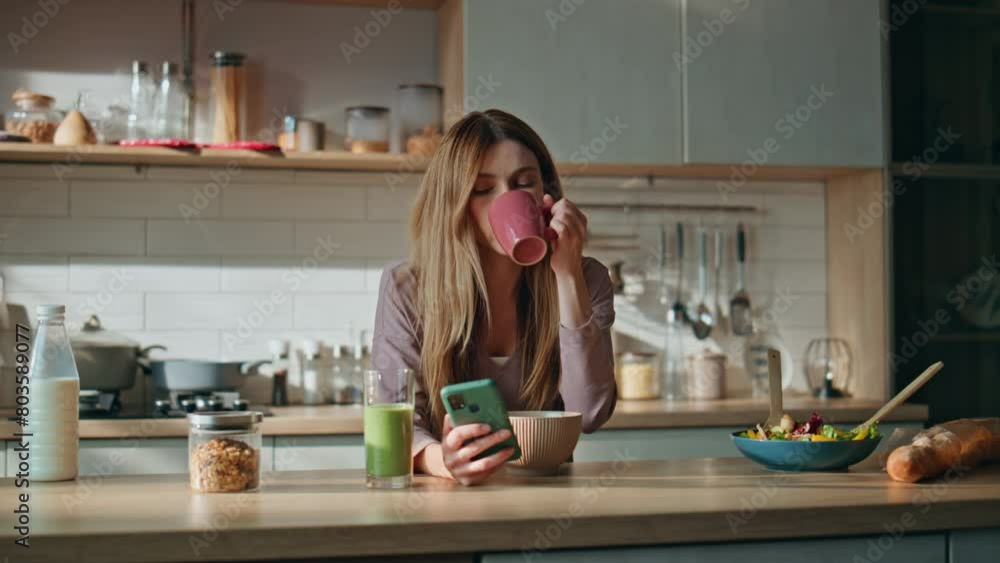 Bored girl chatting smartphone drinking coffee at kitchen. Woman looking phone Bored girl chatting smartphone drinking coffee at kitchen. Woman looking phone