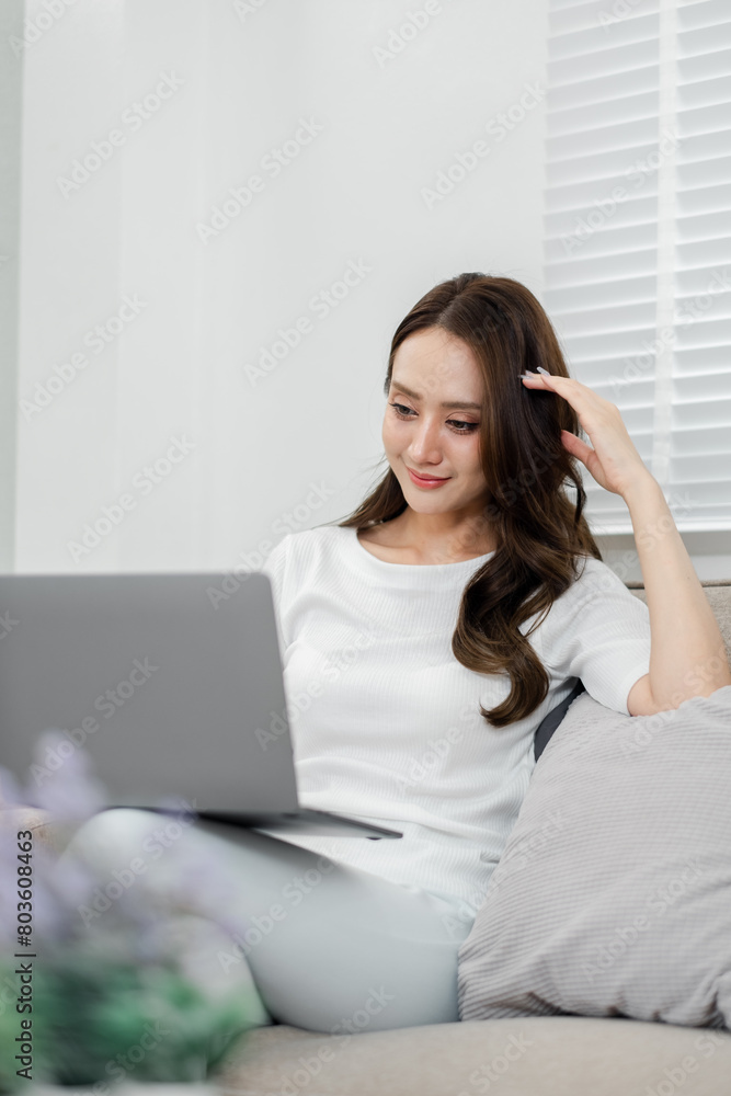 Thoughtful woman lounging with a laptop, enjoying some quiet time in the soft light of her peaceful home. Thoughtful woman lounging with a laptop, enjoying some quiet time in the soft light of her peaceful home.