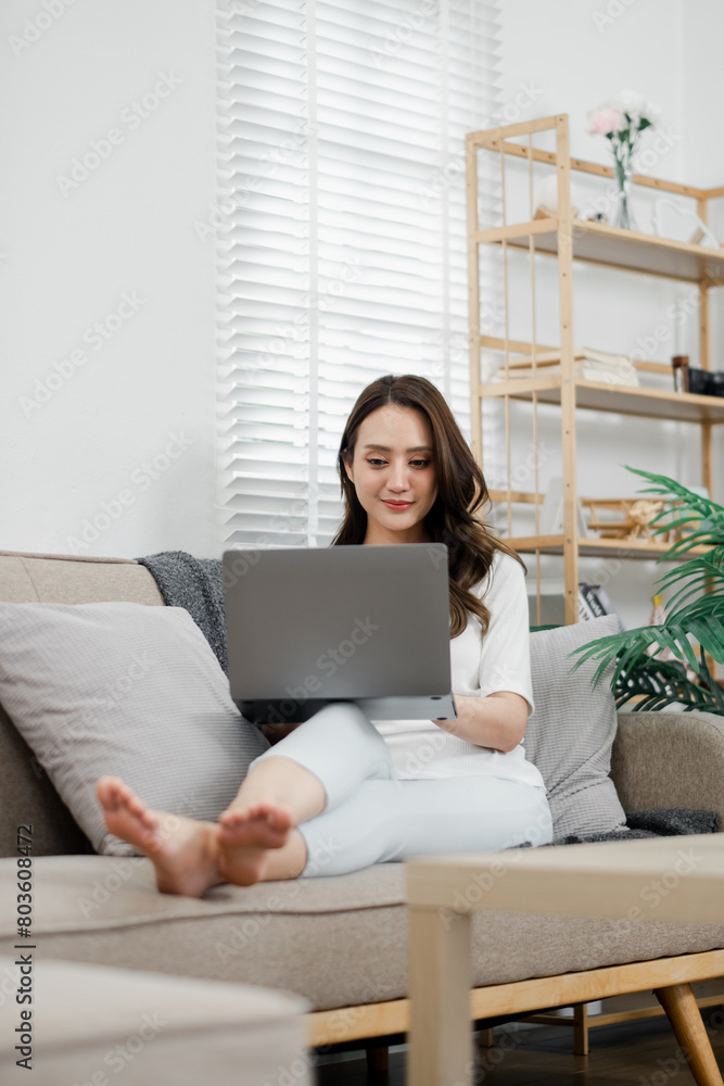 Woman in a casual setting comfortably browsing on her laptop, with natural light streaming through the window of her tidy living room. Woman in a casual setting comfortably browsing on her laptop, with natural light streaming through the window of her tidy living room.