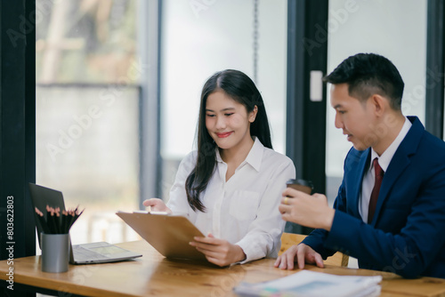 A man and a woman are sitting at a table with a laptop and a cup of coffee