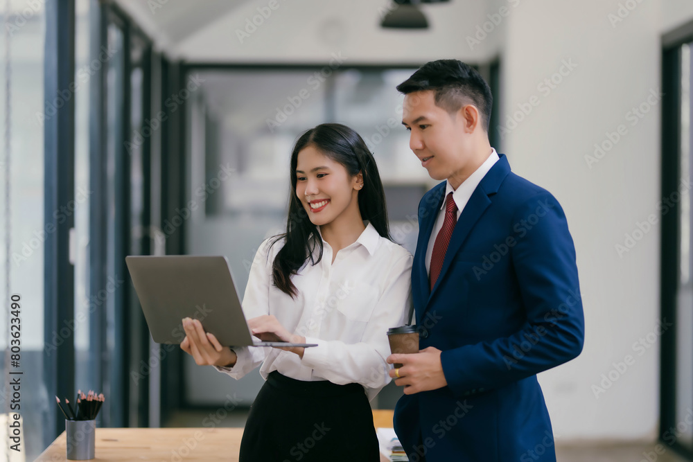 A woman and a man are standing in a room, looking at a laptop