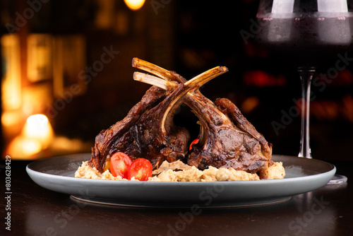 grilled rack of lamb with potato compote paired with glass of red wine on wooden table photo