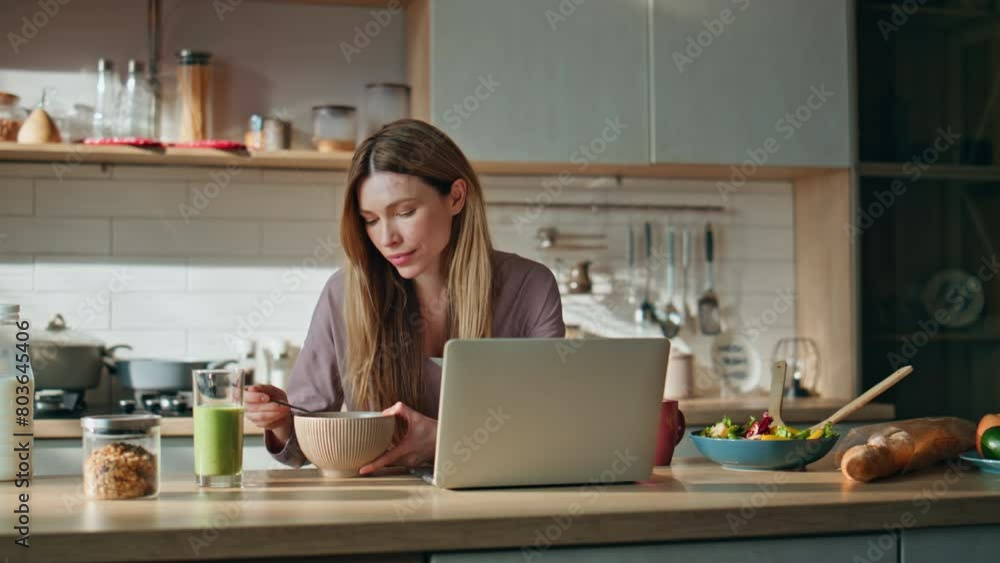 Breakfasting woman looking laptop screen on kitchen. Relaxed girl eating food Breakfasting woman looking laptop screen on kitchen. Relaxed girl eating food