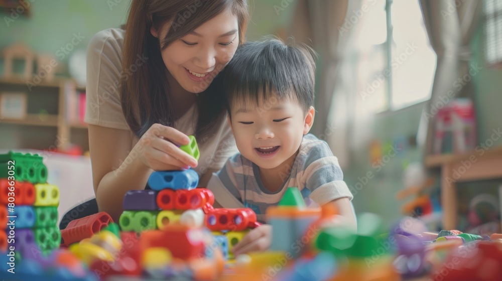 Fototapeta premium Asian young boy is playing with a stack of colorful blocks while his mother watches.
