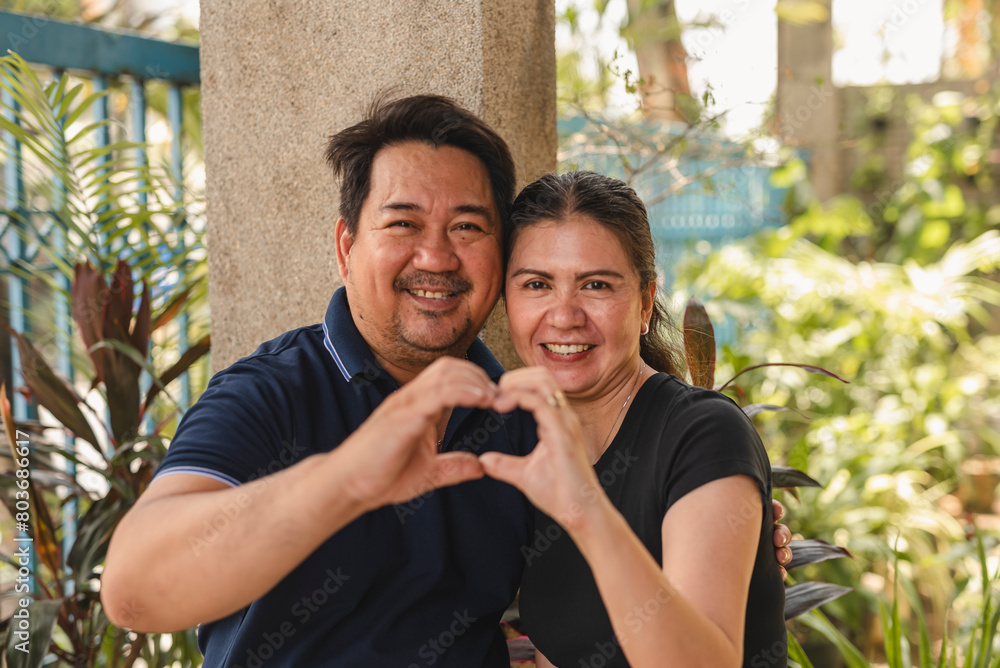 Fototapeta premium Middle aged Southeast Asian couple creates a heart with their hands, symbolizing love and two decades of togetherness.