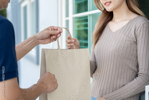 Happy smiling Asian woman receives paper bag parcel of food from courier front house. Delivery man send deliver express. online shopping, paper container, takeaway, postman, delivery service, packages © Shisu_ka