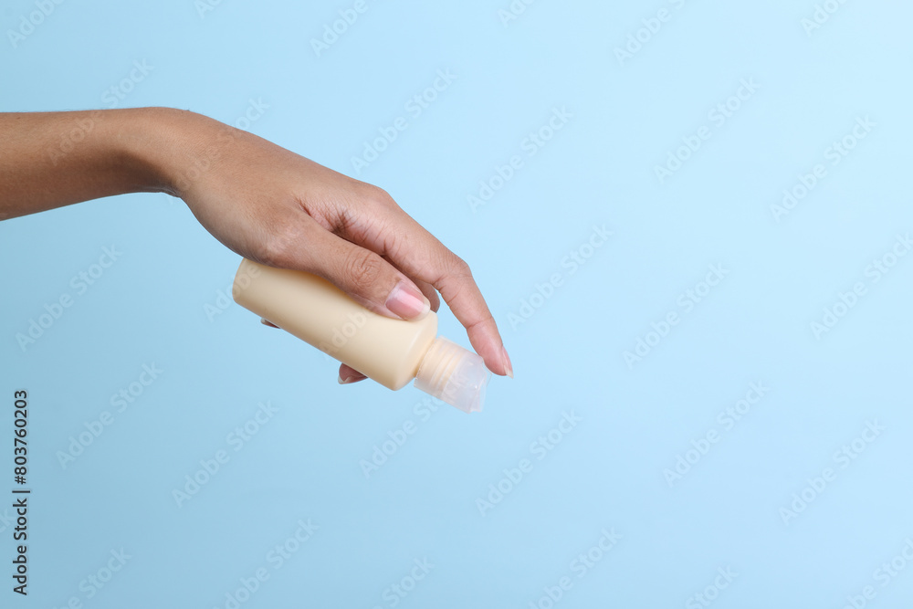 Woman hand holding yellow blank small spray bottle mockup isolated on blue background Woman hand holding yellow blank small spray bottle mockup isolated on blue background