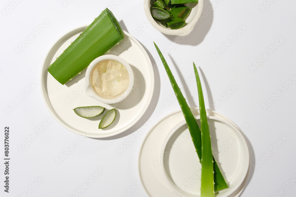 Top view of aloe vera decorated contained on several white porcelain dishes flat lay on white flat form. Photo for advertising product made by aloe, blank space for design Top view of aloe vera decorated contained on several white porcelain dishes flat lay on white flat form. Photo for advertising product made by aloe, blank space for design