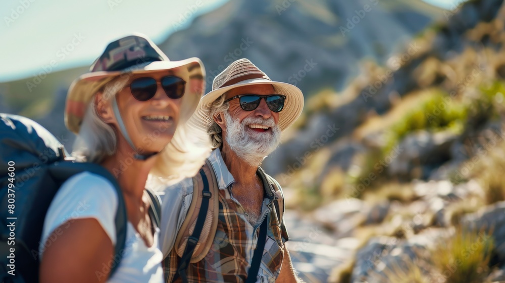 A happy and active senior couple hiking in the mountains. They are both smiling and enjoying the scenery. The man is wearing a hiking hat and backpack A happy and active senior couple hiking in the mountains. They are both smiling and enjoying the scenery. The man is wearing a hiking hat and backpack