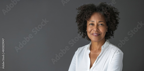 A smiling middle-aged black woman with short curly hair is wearing a white shirt on a grey background, looking at the camera.