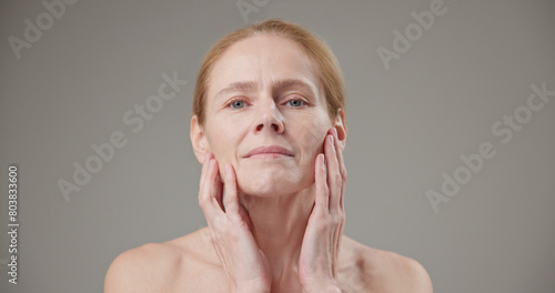 Real people age, beauty, health and dry skin care concept - beautiful mature Caucasian middle aged woman in her 50s touching facial skin doing facial massage and looking at camera © Anatoly Repin